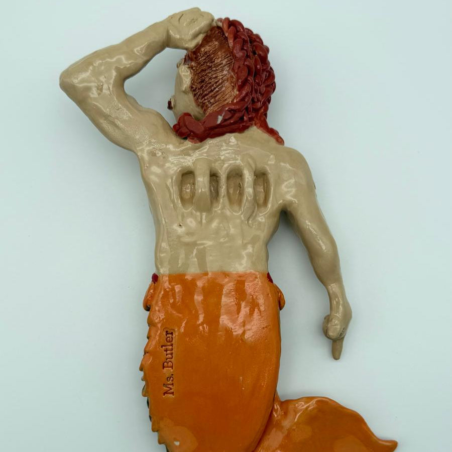 Mermaid figurine with red hair and orange tail on a light blue background