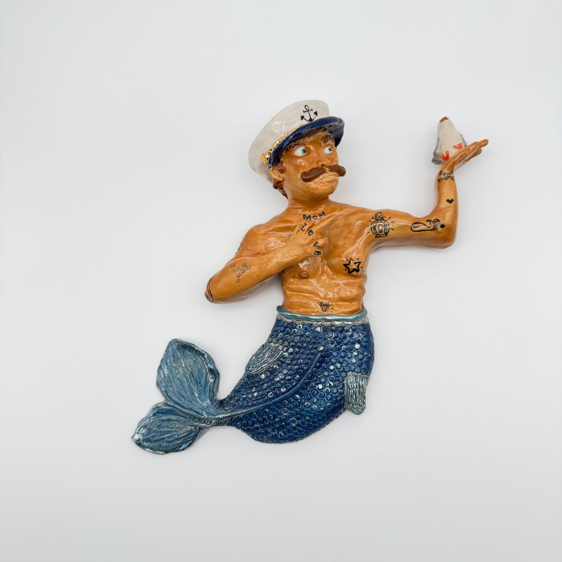 Decorative wall piece of a merman with a captain's hat holding a bird on a white background